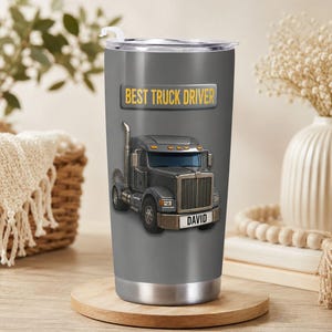May include: A gray stainless steel tumbler with a clear lid and a white straw. The tumbler features a graphic of a gray semi-truck with the text "BEST TRUCK DRIVER" in yellow above the truck and the name "DAVID" printed on the truck's front bumper.