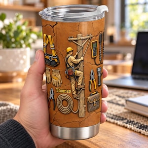 May include: A stainless steel tumbler with a clear lid featuring a graphic of a utility worker climbing a wooden pole. The design includes tools like pliers, a coil of rope, a tool belt, and a bag, set against a cracked brown background with the name Thomas printed in yellow.