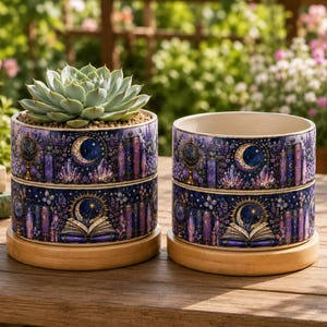 Può includere: Due vasi cilindrici in ceramica con un motivo celeste blu scuro e viola raffigurante lune, libri aperti, cristalli e globi. Ogni vaso poggia su una base circolare in legno chiaro. Un vaso contiene una pianta succulenta verde.