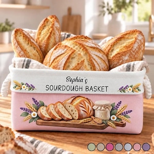 May include: A rectangular fabric storage basket with a light pink base and white top rim. The text reads Sophia's SOURDOUGH BASKET. The front features a graphic of sliced bread, a jar, wheat, and lavender. The basket is filled with four loaves of bread.