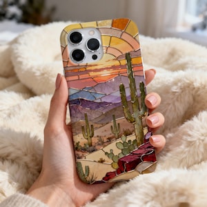 May include: A phone case featuring a desert landscape design with a sunset, mountains, and cacti. The case has a stained glass effect with warm colors like orange, yellow, and red. The design includes a variety of cacti and desert plants.
