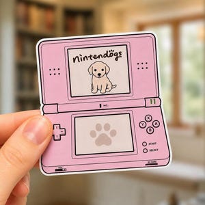 May include: A pink handheld gaming console sticker featuring a top screen with the text Nintendogs and a puppy illustration, and a bottom screen displaying a paw print. The device includes a directional pad, action buttons, and start select labels.