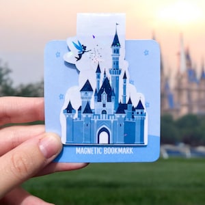 May include: A blue and white magnetic bookmark featuring a silhouette of Cinderella's castle with Tinkerbell flying above. The bookmark has the text "MAGNETIC BOOKMARK" printed on the bottom.