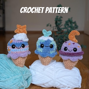 May include: Three crocheted ice cream cone plush toys with different space-themed designs. The ice cream cones are purple, blue, and orange with white crocheted tops. Each cone has a cute face with black eyes and a smiling mouth. The ice cream cones are sitting on a white and blue yarn.