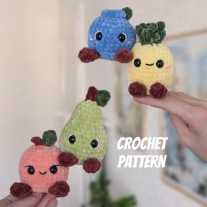 May include: Four plush crochet fruit toys including a blue blueberry, a yellow pineapple, a green pear, and a peach-colored apple. Each toy features dark brown feet, black safety eyes, and embroidered smiles. The text CROCHET PATTERN is visible.
