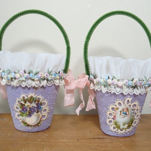 May include: Two lavender-colored Easter baskets with white lace trim and green pipe cleaner handles. Each basket has a white ruffled lining and a vintage-style image of a girl holding an egg.
