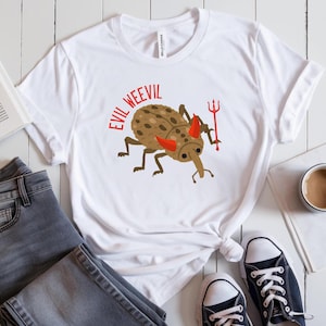 May include: White t-shirt featuring a cartoon weevil in brown and black, sporting red devil horns and holding a red pitchfork. The text "Evil Weevil" is printed above the weevil.