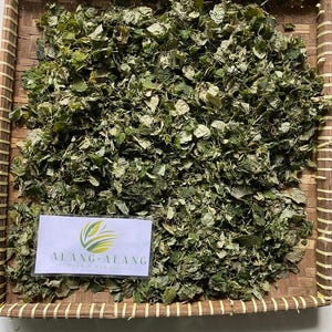 May include: A woven basket filled with dried green leaves. The basket has a label that reads "ALANG-ALANG" in green text.
