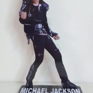May include: A black and white cutout of Michael Jackson in a performance pose. He wears a black outfit with silver accents and a glove. The base reads "MICHAEL JACKSON BAD" in white and red lettering.