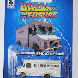 May include: A collectible toy GMC step van in white, packaged on a blue card with lightning graphics. The van features the text DR. E. BROWN ENTERPRISES 24 HR SCIENTIFIC SERVICES. The packaging includes the Back to the Future logo and Milonga Customs branding.