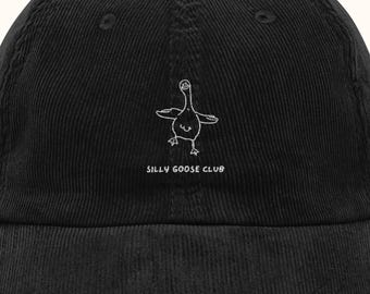 May include: A black corduroy baseball cap featuring an embroidered white line drawing of a goose with its wings spread out. Below the goose, the text SILLY GOOSE CLUB is embroidered in white thread. The cap has a structured crown and a curved brim.