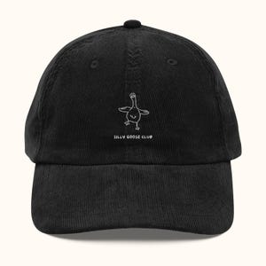May include: A black corduroy baseball cap featuring a white embroidered line drawing of a goose with its wings spread out. Below the goose, the text SILLY GOOSE CLUB is embroidered in white capital letters on the front center of the cap.
