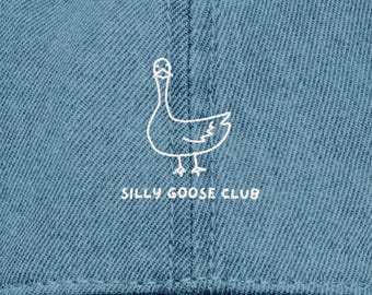 May include: A denim blue baseball cap featuring the words "SILLY GOOSE CLUB" embroidered in white. Above the text is a white outline of a goose. The cap has a curved peak and a small vent hole.