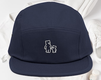 May include: A navy blue five-panel cap featuring a white embroidered graphic of a large bear holding the hand of a small bear centred on the front panel. The hat has a flat brim and a structured crown with stitched eyelets on the side panels.