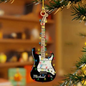 Puede incluir: Adorno navideño en forma de guitarra en blanco y negro con luces de colores. El adorno tiene el nombre "Michael" impreso. Cuelga de un hilo dorado.