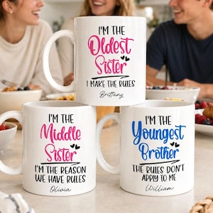 May include: Three white ceramic mugs with black and pink or blue text. The top mug says I'M THE OLDEST SISTER I MAKE THE RULES Brittany. The bottom left says I'M THE MIDDLE SISTER I REASON WE HAVE RULES Olivia. The bottom right says I'M THE YOUNGEST BROTHER THE RULES DON'T APPLY TO ME William.