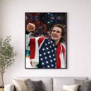 May include: A framed photograph of a smiling person draped in an American flag. The flag features red and white stripes and white stars on a blue background. The person is wearing a white and black uniform and has their fist raised in the air.