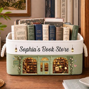 Può includere: Un contenitore rettangolare in tessuto con manici in corda bianca, recante la scritta "Sophia's Book Store" e un'illustrazione di una vetrina verde con due finestre ad arco che mostrano scaffali pieni di vari libri classici con copertina rigida.