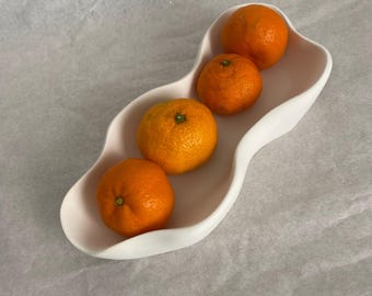 May include: A white ceramic bowl with a wavy design, holding four orange mandarins.