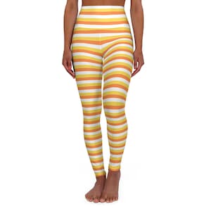 Puede incluir: Leggings de cintura alta con rayas horizontales blancas, amarillas y naranjas. Los leggings son ajustados y llegan a los tobillos. El diseño general es un patrón brillante y alegre.