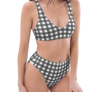 Puede incluir: Conjunto de bikini de dos piezas con estampado de cuadros blancos y negros. La parte superior es de estilo cuello redondo y la braguita de cintura alta ofrece cobertura total. El traje de baño está hecho de una tela suave, probablemente elástica.