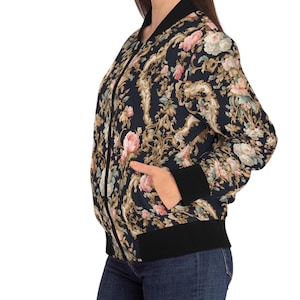 May include: A black bomber jacket with a floral print featuring pink and cream roses and gold accents. The jacket has a zipper closure and ribbed cuffs and hem.