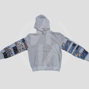 Könnte beinhalten: Ein grauer Kapuzenpullover mit Patchwork-Stoff an den Ärmeln. Der Patchwork-Stoff ist in Blautönen, Braun und Weiß.