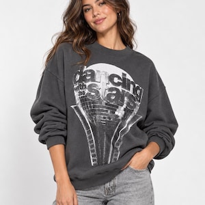 May include: A charcoal gray crewneck sweatshirt featuring a white graphic print of a disco ball and the text Dancing with the Stars. The long-sleeved pullover has a ribbed collar, cuffs, and hem, paired with light gray denim jeans.