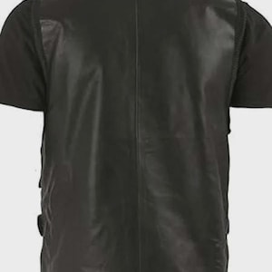 Puede incluir: Un chaleco de cuero negro con un acabado liso y s&oacute;lido, que presenta una costura vertical central en la espalda. La prenda sin mangas tiene un cuello alto y se lleva sobre una camiseta negra de manga corta, mostrando un dise&ntilde;o estructurado.