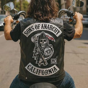 May include: A person riding a motorcycle, wearing a black leather vest with the "Sons of Anarchy" logo and "California" text. The vest features a Grim Reaper graphic. The person is wearing blue jeans.