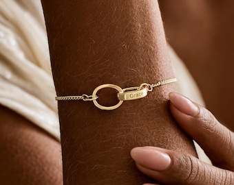 May include: A gold-colored bracelet with an oval-shaped clasp and a delicate chain. The clasp has the name "Grace" engraved on it. The bracelet is worn on a wrist with a light skin tone.