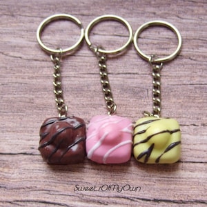 May include: Three keychains with miniature chocolate, pink and yellow cakes attached. Each cake has a different coloured icing and chocolate drizzle.