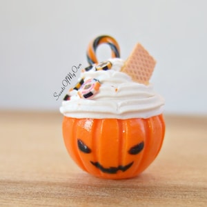 May include: A small orange pumpkin-shaped ornament with a white frosting topping, candy, and a waffle cookie. The ornament is decorated with a black jack-o'-lantern face and the text "Sweets Of My Own".