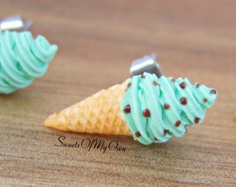 Puede incluir: Un par de pendientes de cono de helado con una bola de helado verde menta y chispas de chocolate. Los pendientes están hechos de arcilla polimérica y tienen postes de plata.