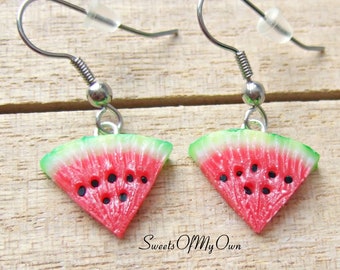 May include: A pair of watermelon slice earrings with silver hooks. The earrings are made of polymer clay and feature a realistic watermelon design with red flesh, black seeds, and green rind.