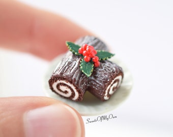 May include: A miniature chocolate yule log cake decorated with green holly leaves and red berries. The cake is on a small white plate.