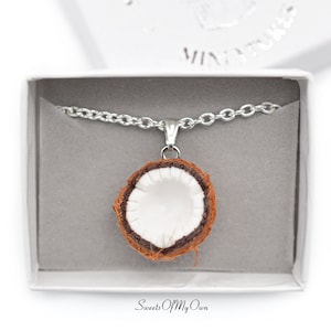 May include: A silver chain necklace with a brown and white coconut pendant. The necklace is in a white box with the words "Sweets Of My Own" printed on the bottom.