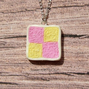 Può includere: Una collana con un ciondolo quadrato rosa e giallo. Il ciondolo è fatto di pasta polimerica e ha una superficie testurizzata. La collana è su una catena d'argento.
