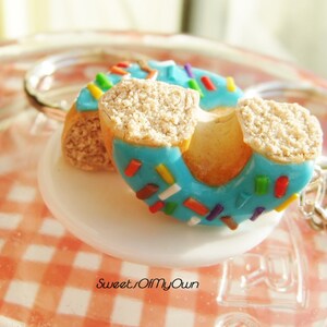 May include: A blue and white donut keychain with colorful sprinkles. The donut is split in half and the keychain is attached to the side.