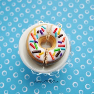 May include: A white frosted donut with colorful sprinkles on a white pedestal. The donut is split in half and has a hole in the middle.