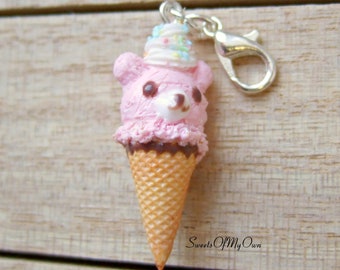 May include: A pink bear-shaped ice cream cone charm with a white and pink ice cream scoop, chocolate sauce, and sprinkles. The charm is attached to a silver lobster clasp.