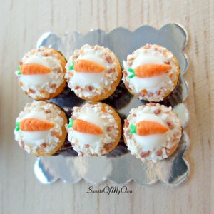 Peut inclure: Six mini cupcakes au g&acirc;teau de carottes avec un gla&ccedil;age blanc et une carotte sur le dessus. Les cupcakes sont sur un plateau argent&eacute; &agrave; bord festonn&eacute;. Le plateau est sur une surface en bois.