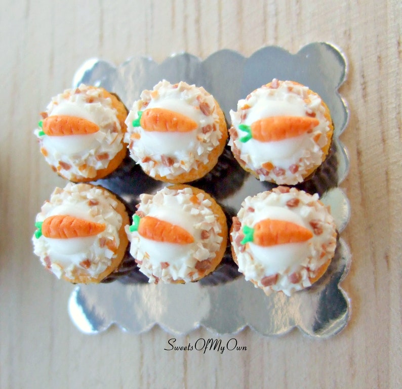 Peut inclure: Six mini cupcakes au g&acirc;teau de carottes avec un gla&ccedil;age blanc et une carotte sur le dessus. Les cupcakes sont sur un plateau argent&eacute; &agrave; bord festonn&eacute;. Le plateau est sur une surface en bois.