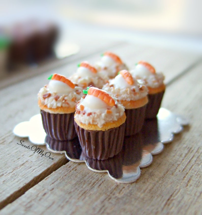 Peut inclure: Gros plan sur six mini cupcakes au g&acirc;teau de carottes avec gla&ccedil;age au fromage frais et un petit bonbon en forme de carotte sur le dessus. Les cupcakes sont dispos&eacute;s sur un plateau argent&eacute; &agrave; bord festonn&eacute;. Le plateau est pos&eacute; sur une surface en bois.