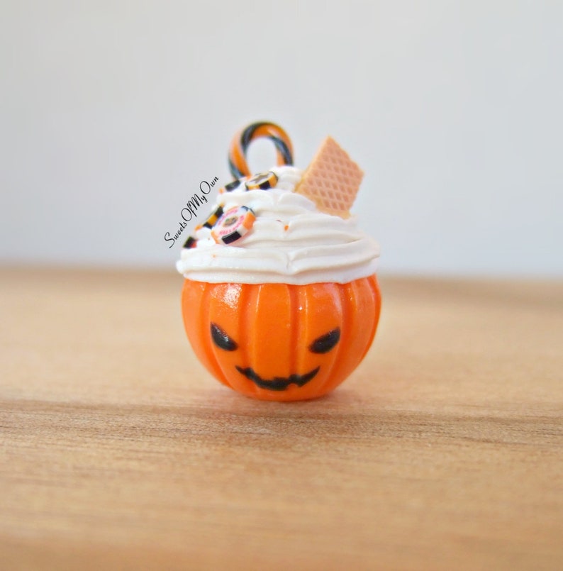 May include: A small orange pumpkin-shaped ornament with a white frosting topping, candy, and a waffle cookie. The ornament is decorated with a black jack-o'-lantern face and the text "Sweets Of My Own".