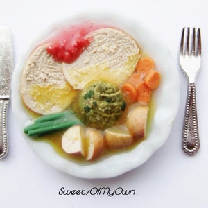 May include: A white plate with a miniature meal of turkey, stuffing, gravy, carrots, potatoes, and green beans. The plate is set with a silver knife and fork.