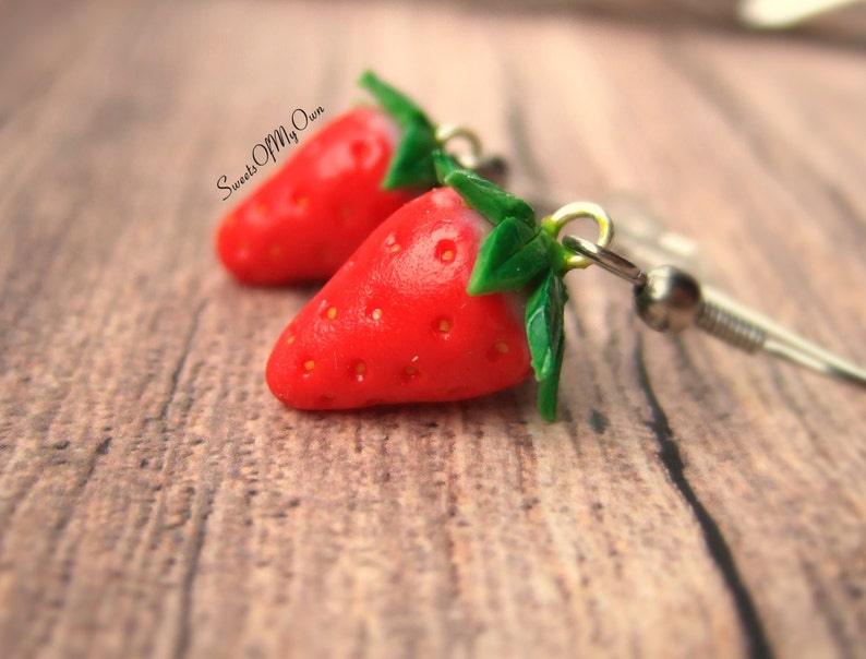 May include: A pair of red strawberry earrings with green leaves, hanging from silver hooks.