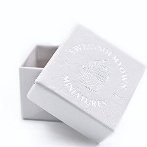 May include: A white box with a silver embossed logo that says "Sweet So  My Own" and "Miniatures" with a cupcake graphic.