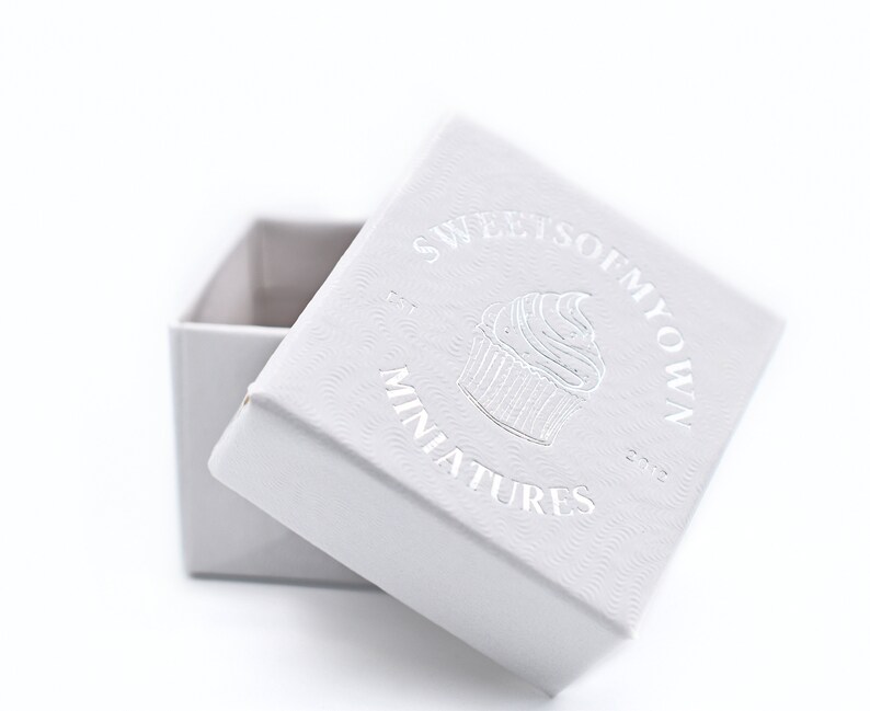 May include: A white box with a silver embossed logo that says "Sweet So  My Own" and "Miniatures" with a cupcake graphic.