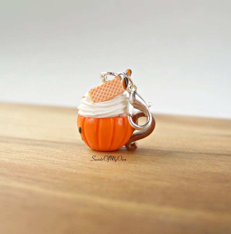 May include: A small orange pumpkin-shaped charm with white frosting and a waffle cookie on top. The charm has a silver clip attached to it.